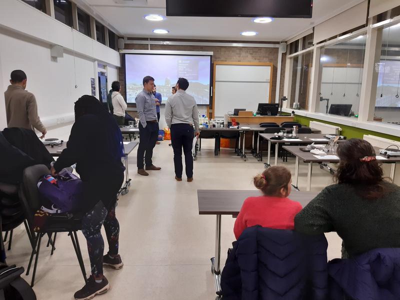 Classroom with several people standing around chatting.