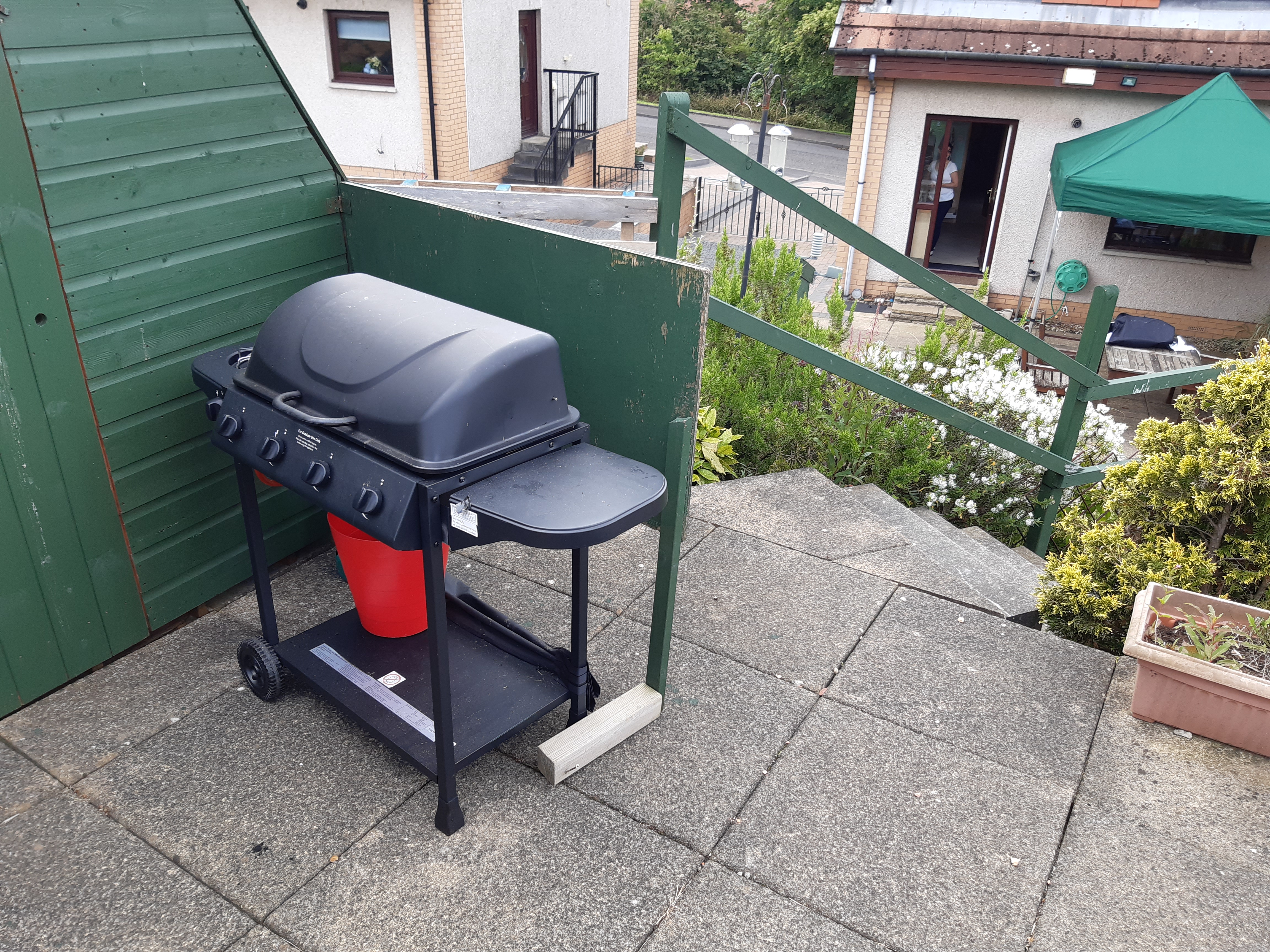 Outside grill with patio and green shelter in background.