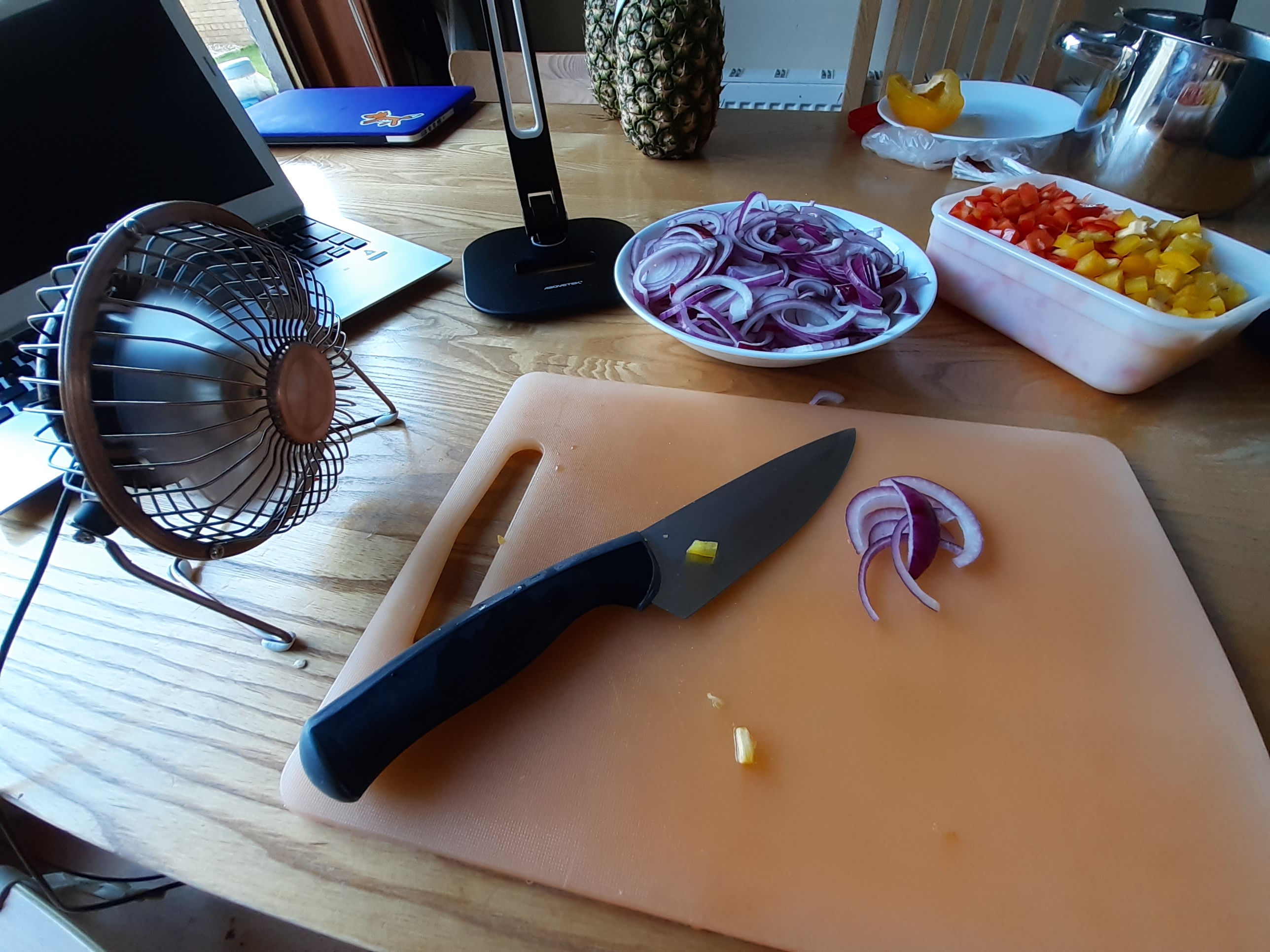 Vapours be gone! Chopping board with knife and sliced red onions. A small fan is sitting to the left.