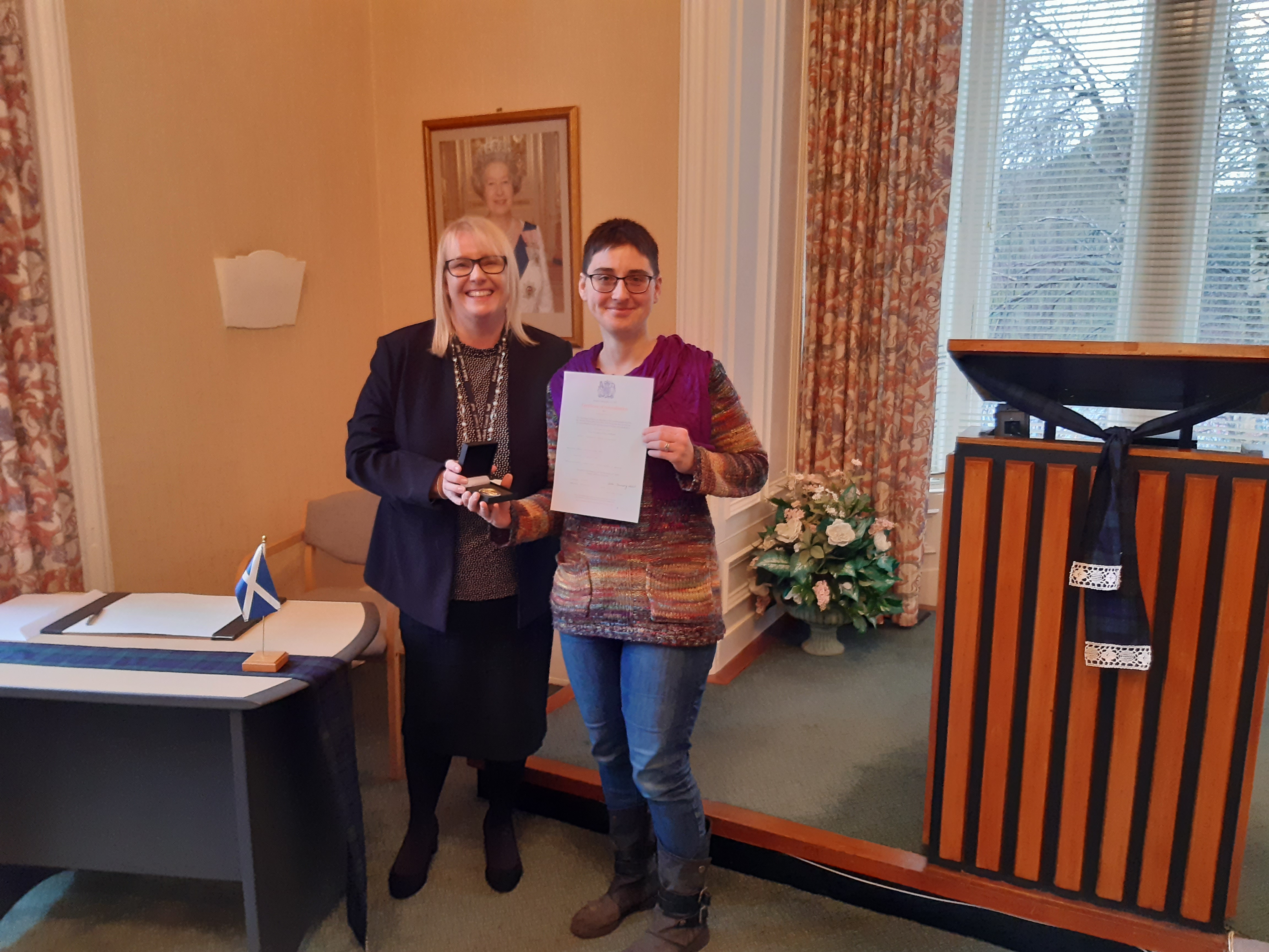 Registrar handing medal and certificate to Denise