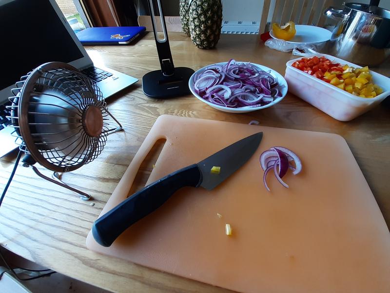 Chopping board with knife and sliced red onions. A small fan is sitting to the left.